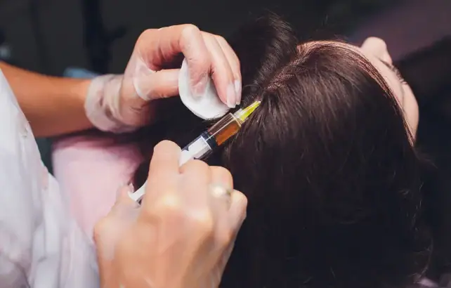 Medical professional administering an injection to a patient's scalp.