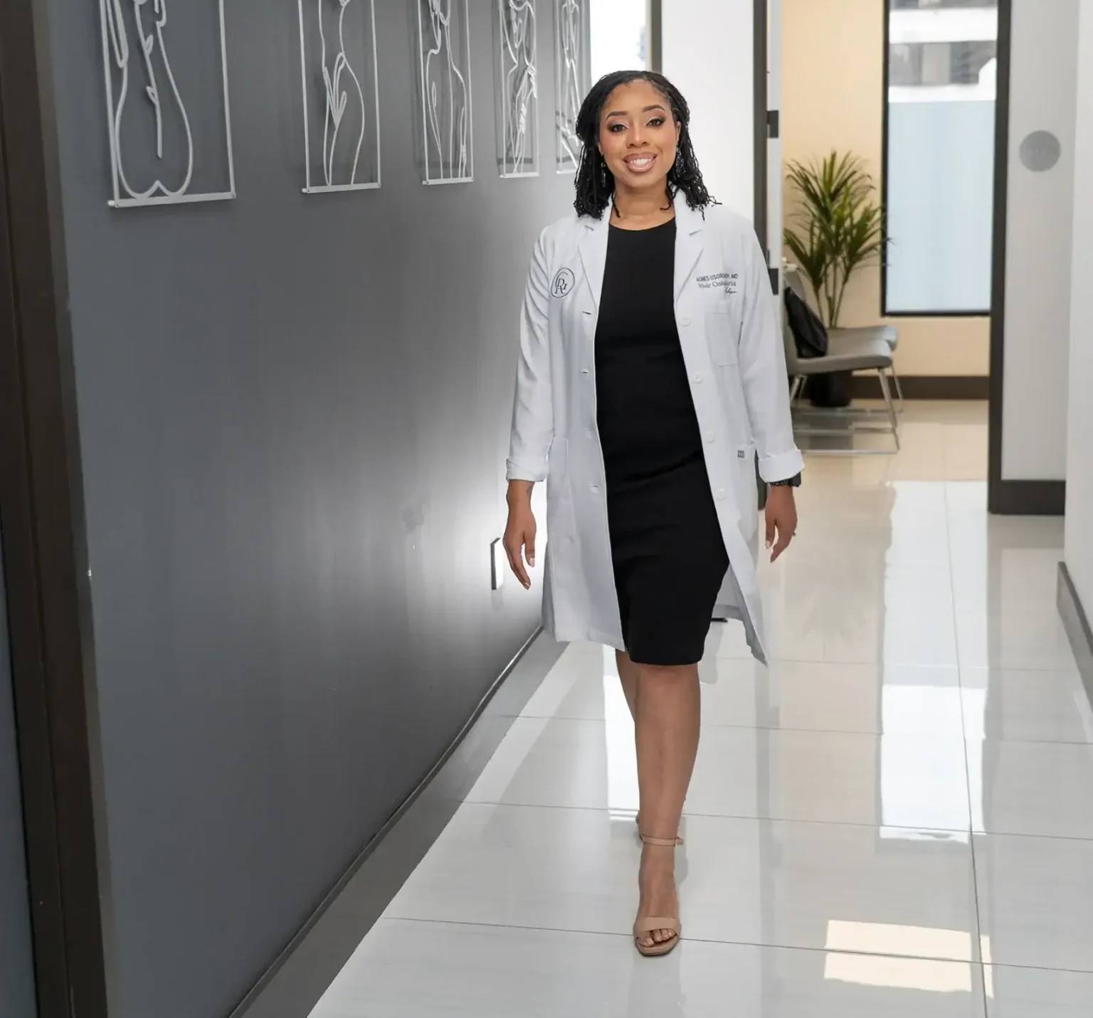 A woman in a white medical coat walking down a modern hallway.