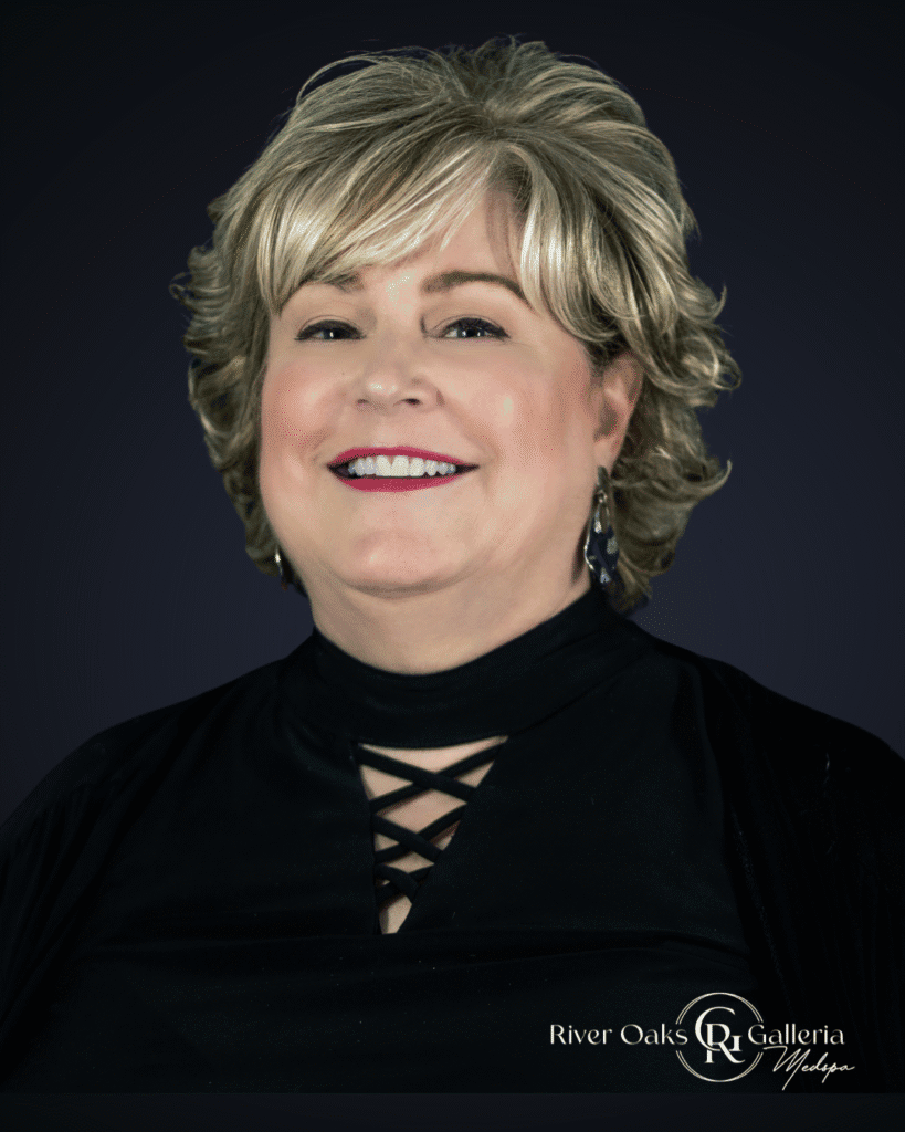 Portrait of a smiling woman with short blonde hair, wearing a black top with lace-up detail.