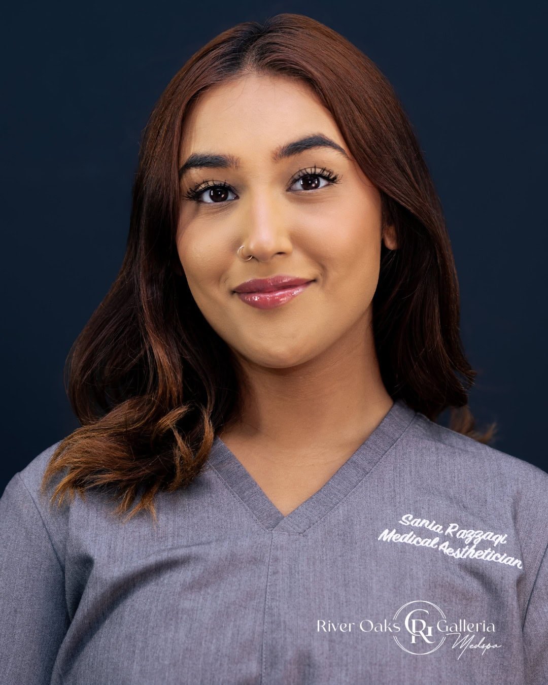 Portrait of a young woman in medical scrubs with "Sania Raggap" embroidered on it.